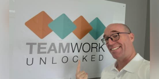Brian in front of the Teamwork Unlocked logo